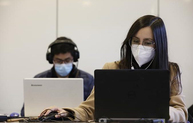 Estudiantes concentrados frente a su computador, estos cuentan con audifonos y tapabocas