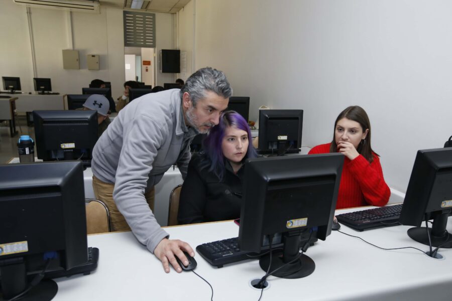 profesor enseñando computación junto a dos alumnas